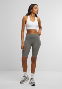 Weißer Sport-BH und graue, hochtaillierte Radshorts, glattes Material, enganliegendes Design, knielange Shorts, kombiniert mit grauen Sportschuhen.
