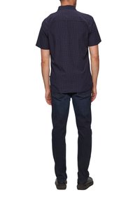 Kortarmig, marineblauw geblokt shirt met een standaardkraag en een boxy fit, gecombineerd met donkere jeans en zwarte schoenen. Achteraanzicht weergegeven.