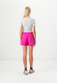 Grått, figurnära kortärmat linne i kombination med rosa, elastiska shorts. Modellen står barfota och visar texturerade strumpor och avslappnade skor.