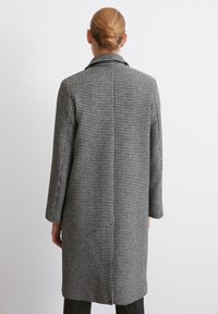 Cămașă cu model houndstooth alb-negru, cu guler crestat, croi drept și mâneci lungi. Prezintă un design de lungime medie și o potrivire ajustată.