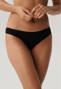 Czarny dół bikini wykonany z elastycznego materiału. Posiada niski stan oraz cienką gumkę w talii, a także minimalne zakrycie z tyłu. Brak widocznych wzorów.