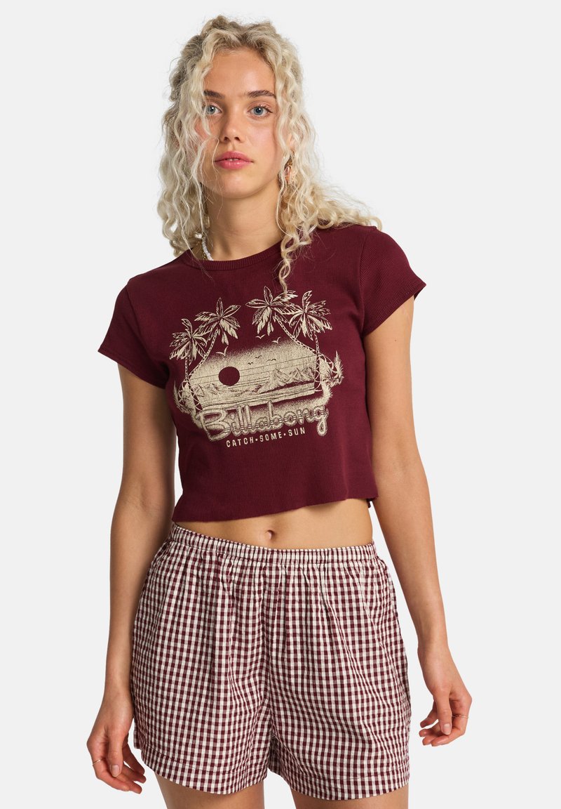 Bordeauxrotes kurz geschnittenes T-Shirt mit Palmenmotiv und Schriftzug; kombiniert mit hoch taillierten Shorts in Bordeauxrot und Weiß kariert. Baumwollmischgewebe.