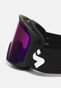 Ochelari de schi negri cu lentile violet, având o curea texturată și umplutură moale în jurul ramei. Detaliu notabil al logo-ului pe curea.