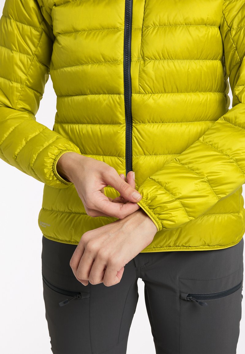 Limettengrüne Pufferjacke mit strukturiertem Finish, ausgestattet mit einem schwarzen Reißverschluss und elastischen Bündchen. Der Träger passt das Bündchen an.