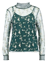 Blouse verte transparente à manches longues, broderie florale, col haut volanté et poignets texturés. Présente un design en couches et des détails délicats.