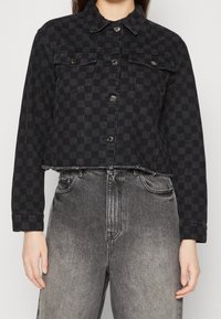 Black and dark gray checkered cropped denim jacket with buttons over faded gray high-waisted jeans.