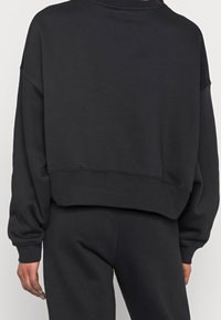 Sudadera negra recortada con hombros caídos, puños elásticos y textura suave. Diseño sencillo, adecuado para uso informal.