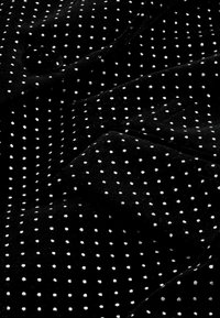 Tissu noir à pois blancs, surface texturée avec un léger éclat. Le tissu est légèrement froissé, mettant en valeur de manière uniforme le motif à pois.