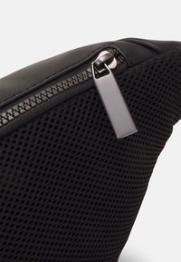 Borsa nera con design a rete testurizzata, bordi in pelle liscia e zip metallica, che enfatizzano funzionalità e durata.