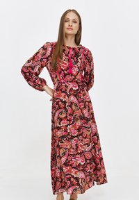 Maxi dress with long sleeves, featuring a vibrant pink and black paisley pattern, tie neckline with tassels, and a flowy silhouette.