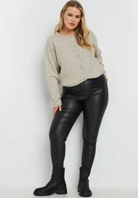 Beige stickad knapp-up kofta, svarta faux läder leggings och svarta anklar stövlar med en kraftig sula, visade på en neutral bakgrund.