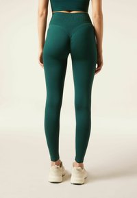 Högmidjade, mörk teal leggings gjorda av stretchigt tyg, med en samlad söm på baksidan och i kombination med ljusa sneakers.