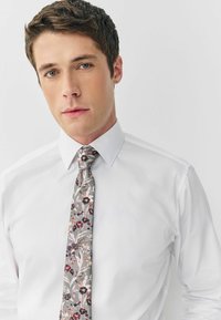 Biała koszula z kołnierzykiem w szpic, w połączeniu z szarym krawatem w kwiaty z różowymi i czarnymi akcentami, gładki materiał i smukły krój.