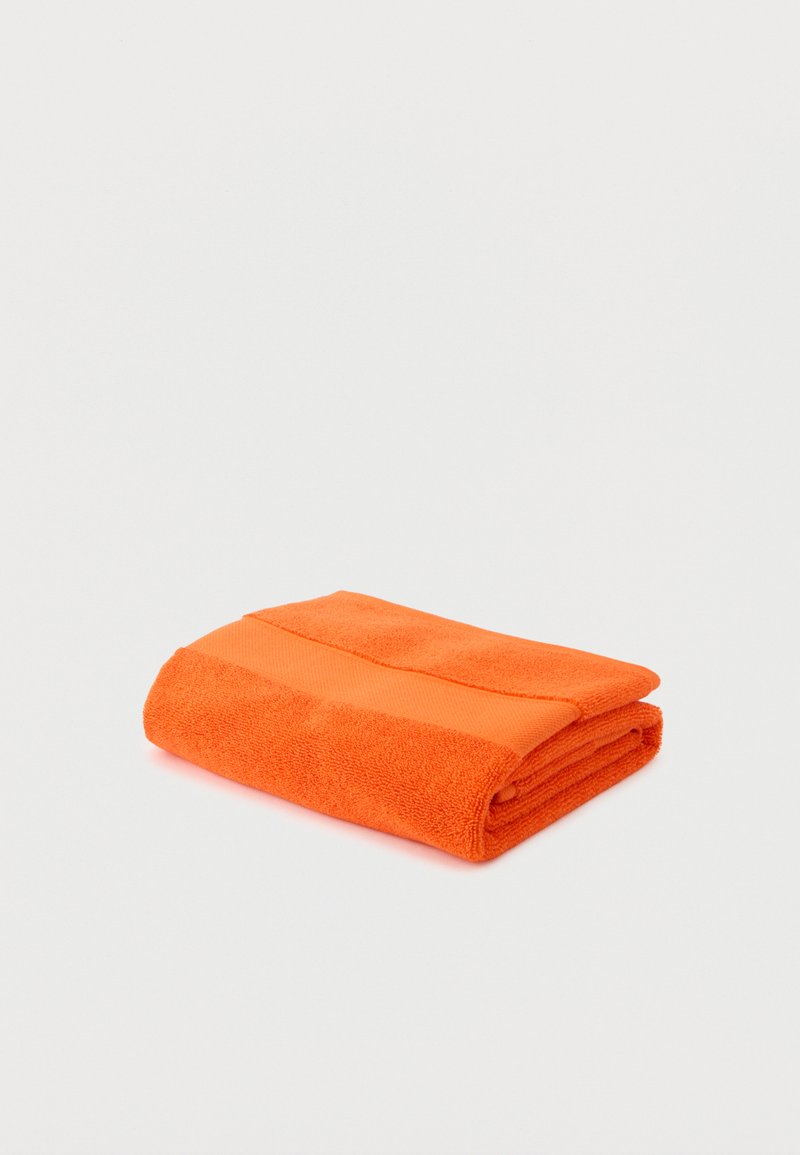 Serviette orange vif pliée avec une bande texturée, présentée sur un fond blanc uni.