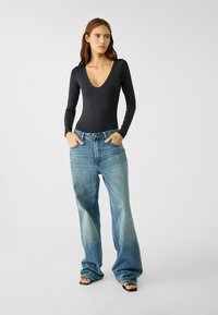 Schwarzer Langarm-Body mit tiefem V-Ausschnitt, kombiniert mit weit geschnittenen, ausgebleichten blauen Jeans. Das Outfit hat einen lässigen Schnitt und ein minimalistisches Design.