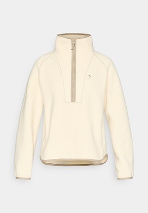 Polaire couleur crème avec une fermeture éclair à moitié sur le devant, bordure contrastante beige, col montant, et détails cousus. Tissu doux et texturé.