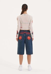 Blusa blanca de manga larga con diseños florales; pantalones cortos de mezclilla anchos azules con cerezas rojas bordadas y el texto "Ed Hardy" en la parte trasera.