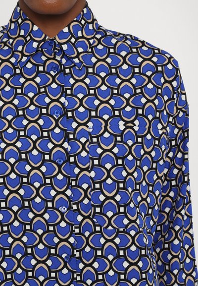 Blue patterned shirt featuring a geometric design with black accents, a classic collar, and blue buttons. Smooth texture, fabric detail visible.