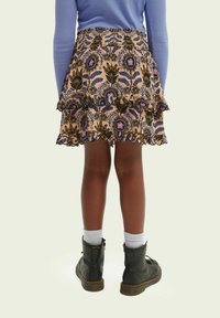 Blomstermønstret, lagdelt nederdel i beige med sorte og lilla accenter, med elastisk taljebånd og bølget kant. Bruges med sorte støvler.