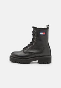 Bottines en cuir noir avec une finition texturée, bout rond, lacets à l'avant et semelle épaisse et robuste. Présente un patch logo sur le côté.