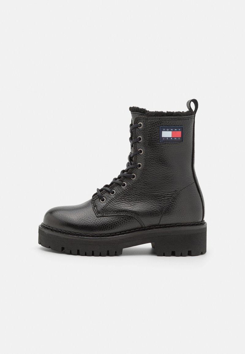Bottines en cuir noir avec une finition texturée, bout rond, lacets à l'avant et semelle épaisse et robuste. Présente un patch logo sur le côté.
