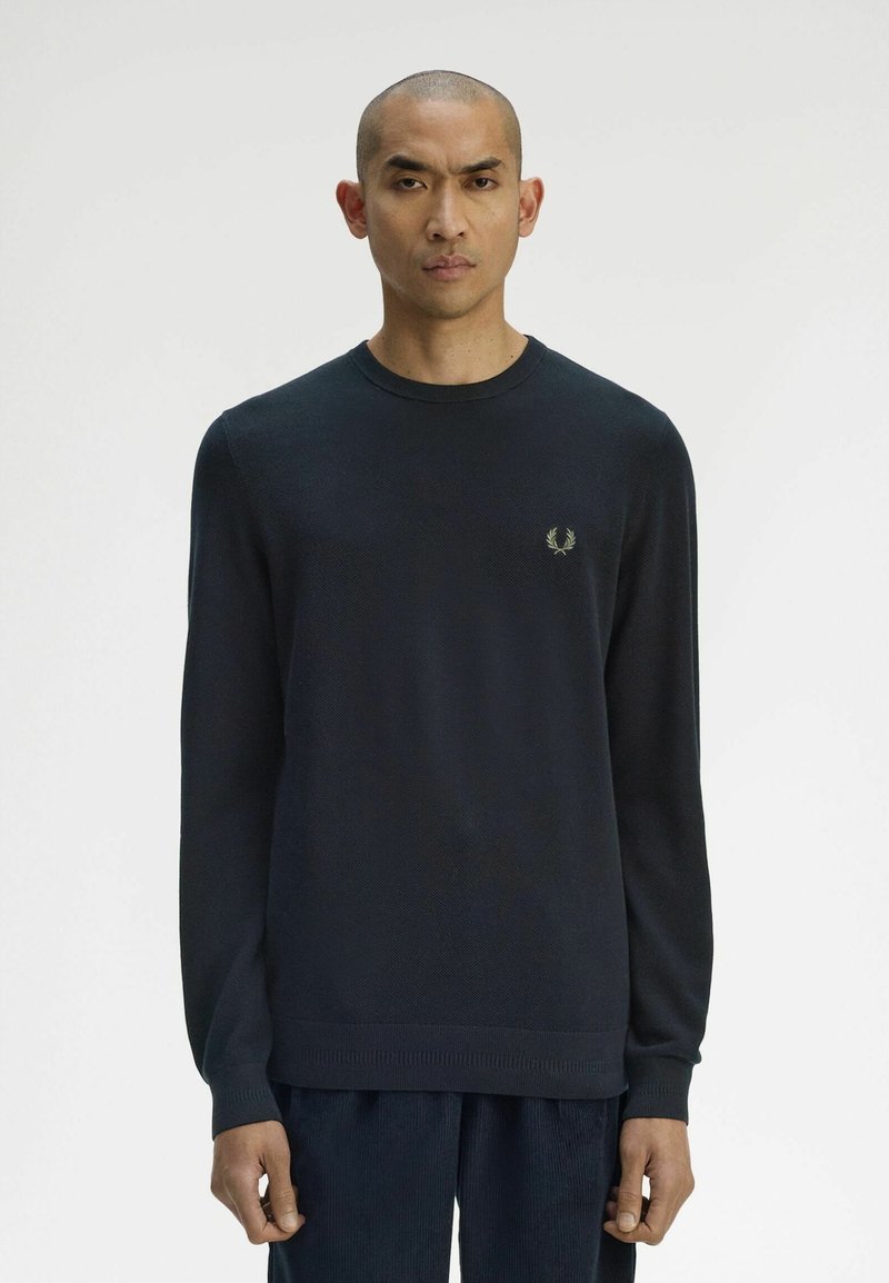 Pull en tricot bleu marine, col rond, manches longues, avec un petit emblème vert sur la poitrine gauche, fabriqué en matériau doux avec des poignets côtelés.