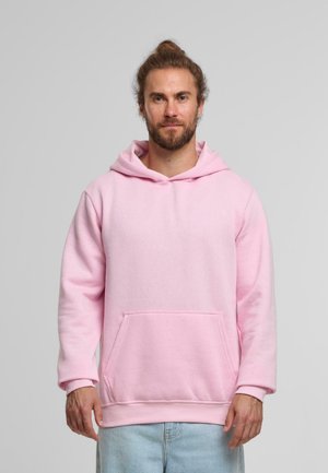 Pink hoodie made of soft fabric, features a front pocket, large hood, and ribbed cuffs. Worn over light blue jeans.