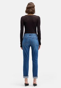 Chemise noire à manches longues ajustées, associée à un jean en denim bleu clair, avec des revers retroussés, une coupe droite et des poches arrière.