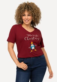 Bordeaux T-shirt met een V-hals, met een speelse pinguïn graphic en de tekst "Vrolijk Kerstfeest" in witte cursieve letters. Korte mouwen.