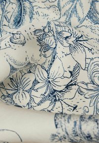 Tejido de algodón con un patrón floral azul sobre un fondo crema, con un detallado trabajo de líneas y una apariencia suave y texturizada.