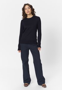 Jūras zila dzija džemperis ar garām piedurknēm, ribotām aprocēm un apaļu kakla izgriezumu, apvienots ar tumši zilām plati kājām biksēm un leoparda raksta apaviem.