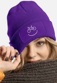 Purple knit beanie with a snug fit, featuring a white bicycle graphic and a smile design on a patch. Textured fabric provides warmth.