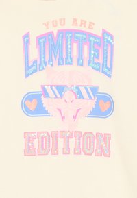 Ein cremefarbener Stoff zeigt ein grafisches Design mit dem Text "DU BIST EINE LIMITIERTE AUFLAGE" in glitzerndem Blau und Pink, akzentuiert durch einen stilisierten Tiger, der Sonnenbrillen trägt.