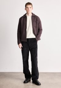 Καφέ ανδρικό σακάκι από μείγμα μαλλιού με γιακά, από μέσα ριγωτό κρεμ πουλόβερ και μαύρο παντελόνι από κορντόνι. Μαύρα παπούτσια ολοκληρώνουν την εμφάνιση.