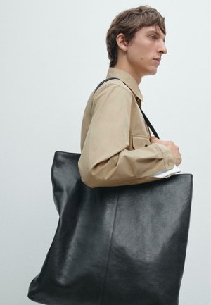 Sort læder tote taske med en glat tekstur, der har et enkelt, minimalistisk design og en enkelt skulderrem.