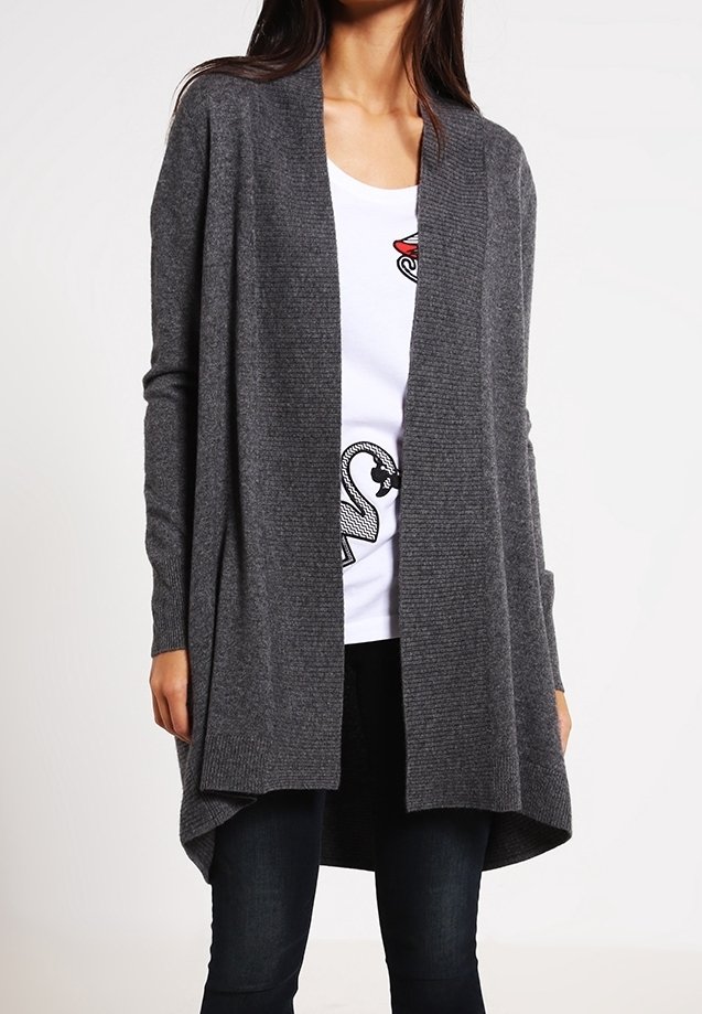 Cardigan gris à ouverture frontale, fabriqué en tissu tricoté texturé, avec des manches longues et un ourlet fluide et asymétrique. Porté sur un t-shirt blanc.