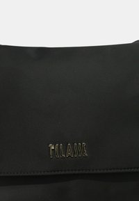 Borsa nera in nylon con una superficie liscia. Presenta una patta anteriore e un logo metallico "TCLASSE" con finitura testurizzata nella parte inferiore.