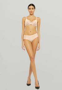 Nude bh och matchande högmidjade underkläder i ett smidigt, elastiskt tyg med en subtil lyster och sömlös design. Svarta högklackade skor.