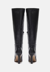 Bottes noires en cuir montant jusqu'au genou avec un tige élégante, un talon aiguille haut, des zippers latéraux et une texture lisse. Design classique avec des accents minimalistes.