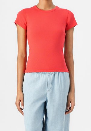 Czerwony prążkowany top z krótkim rękawem i okrągłym dekoltem, w połączeniu z jasnoniebieskimi luźnymi spodniami, tworzący swobodny strój.