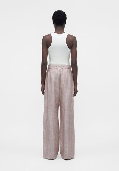Άτομο που φαίνεται από πίσω, φοράει ένα λευκό ριμπ τοπ χωρίς μανίκια και φαρδιά, ριγέ παντελόνια με ροζ χρώμα και ψηλή μέση.