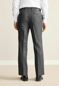 Gray tweed trousers with a straight cut, featuring two back pockets with buttons. Worn with a white long-sleeve shirt and black shoes.