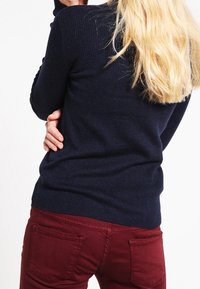 Granatowy sweter z długim rękawem o zwężającym się kroju, w zestawieniu z bordowymi spodniami z tylnymi kieszeniami i teksturowanym wykończeniem.