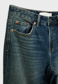 Tmavě modré džíny z denimu s mírným vyblednutím, pět kapsový design, měděné nýty a kontrastní švy v oblasti pasu.