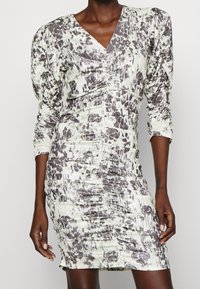 Vestido ajustado de longitud a la rodilla con un patrón abstracto en blanco y negro, detalles fruncidos, escote en V y mangas abullonadas de tres cuartos en un modelo de piel oscura.