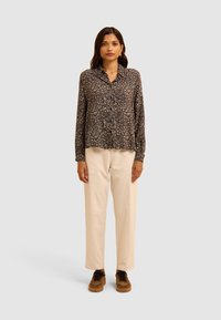 Zwarte bloemetjes langemouwen shirt met een kraag, gecombineerd met crèmekleurige wijde broek en bruine schoenen met een luipaardprint.
