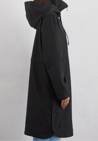 Svart vattentät parka med huva, långa ärmar, tryckknappar och sidofickor. Materialet har en slät, matt textur.