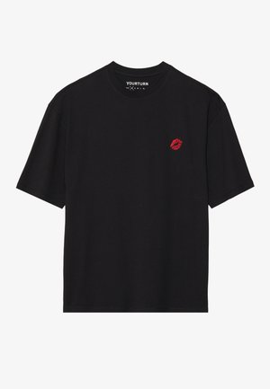 Black short-sleeve t-shirt made of cotton. Features a red lip print on left chest and a crew neckline. Smooth texture and relaxed fit.