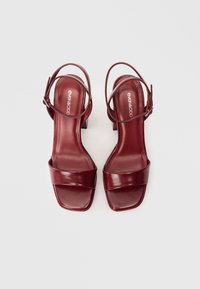 Sandale cu toc burgund cu design pătrat, finisaj lucios și curea ajustabilă la glezna. Dispune de un toc bloc pentru stabilitate.