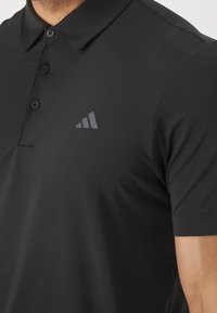 Black polo shirt with a smooth texture, featuring a three-button placket and a small, gray triangular logo on the left chest area.